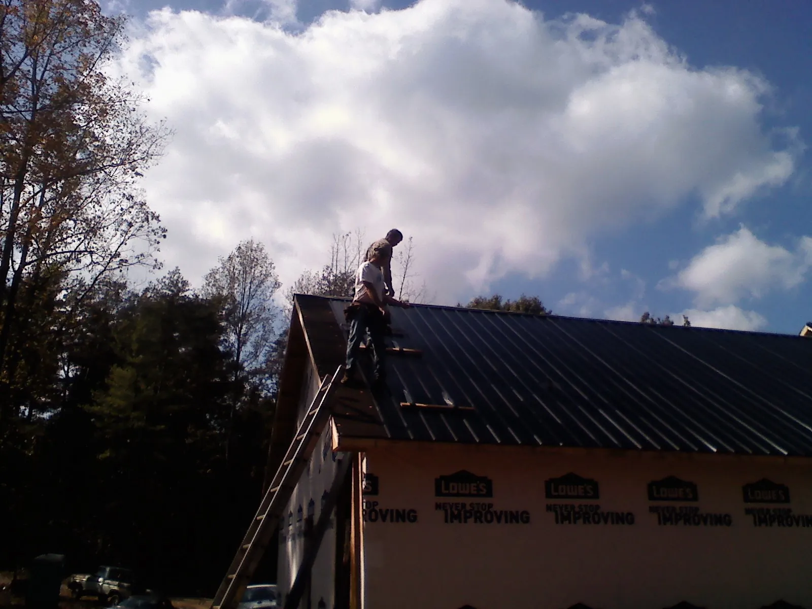 Roofer fastening dark metal panels high against a cloudy sky, from a Roof Inspection job in Braidwood