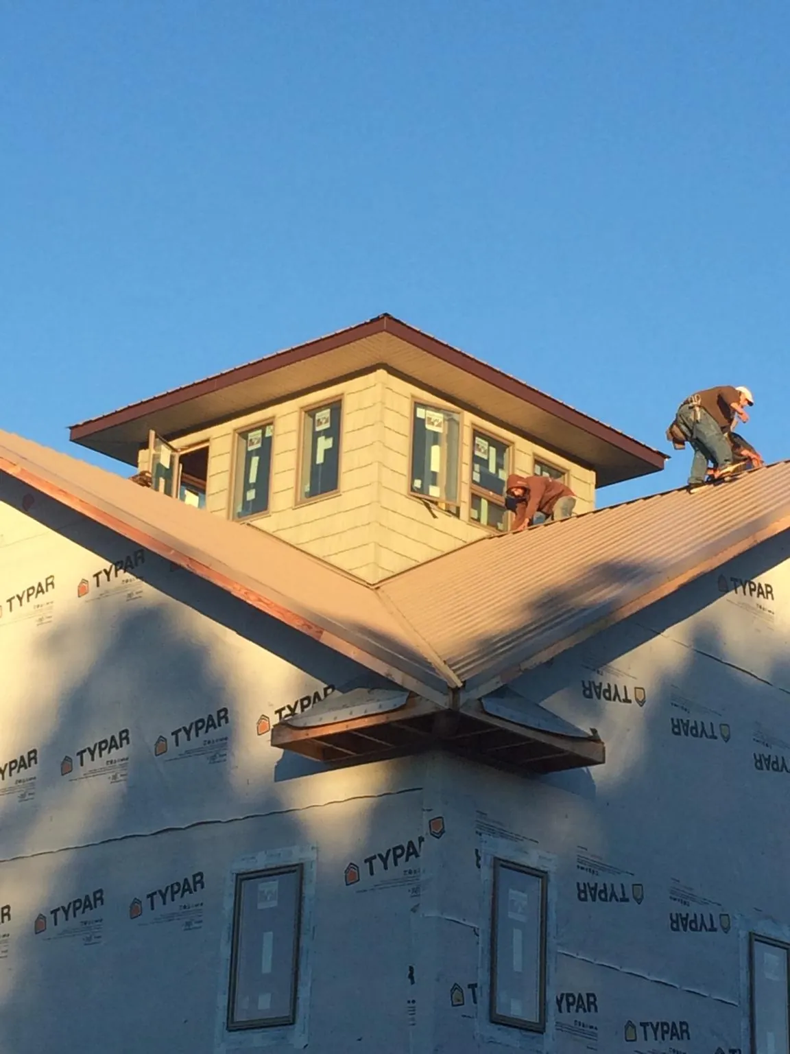 Roofers working around a rooftop cupola on a new metal roof at sunset — Roof Waterproofing in Braidwood by Roofing Brothers